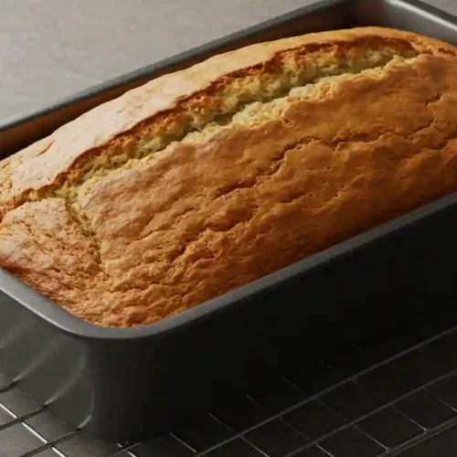 Banana bread doré et moelleux dans un moule à cake noir, posé sur une grille de refroidissement.