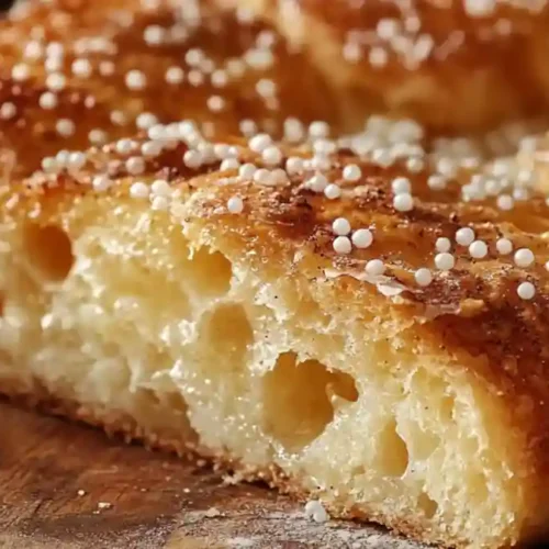 Pain à la Grecque doré saupoudré de sucre perlé sur une planche en bois.